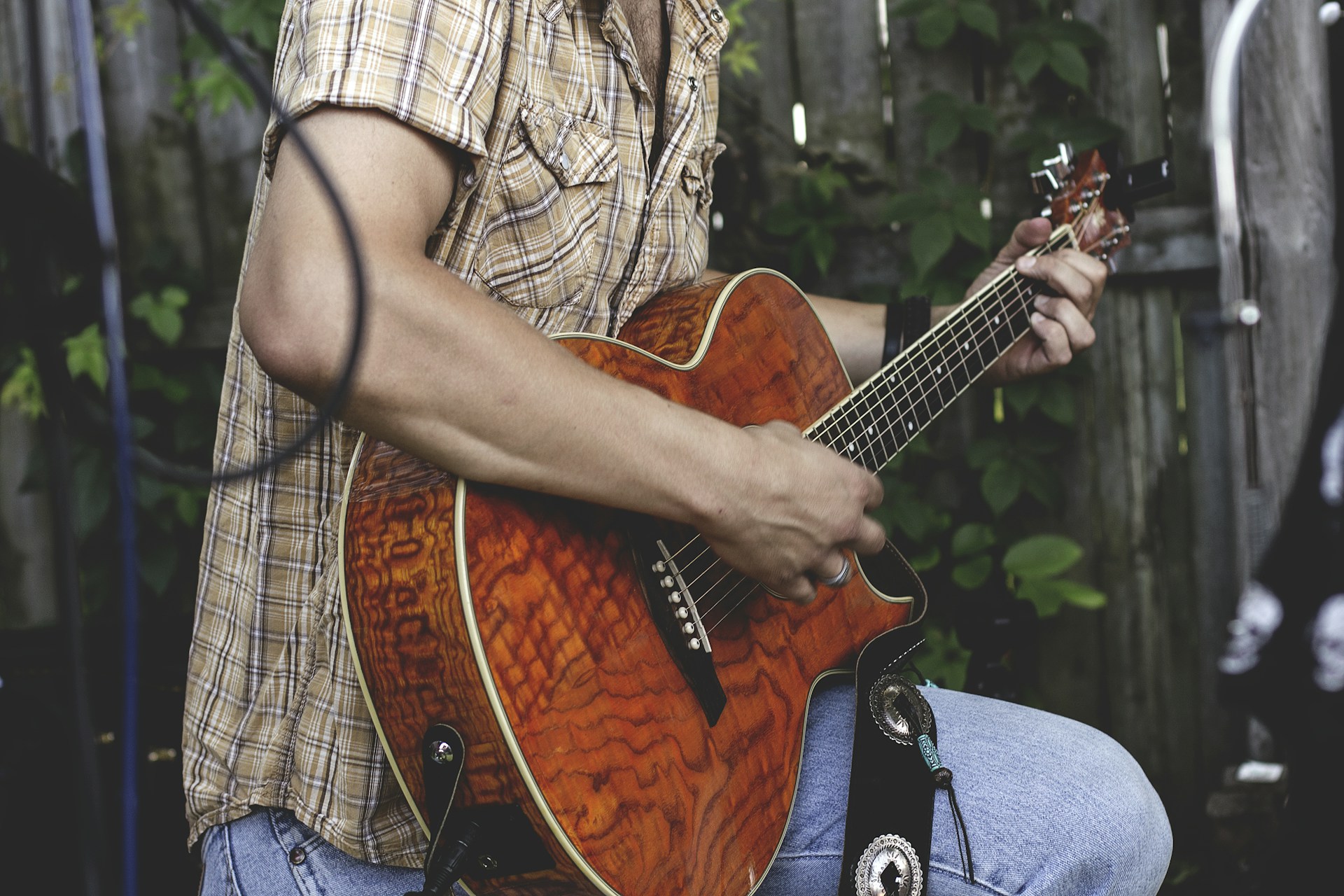 A musician playing acoustic guitar outdoors in natural light