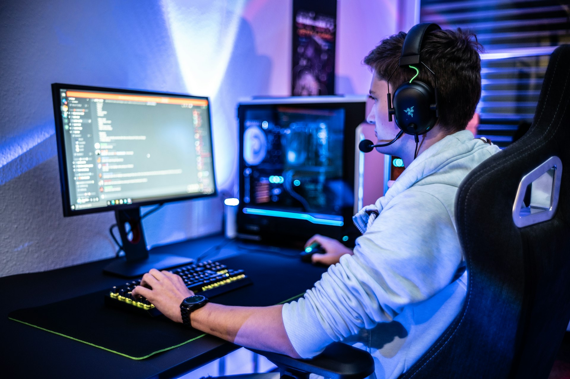 Man wearing gaming headset sitting at computer desk in dark room